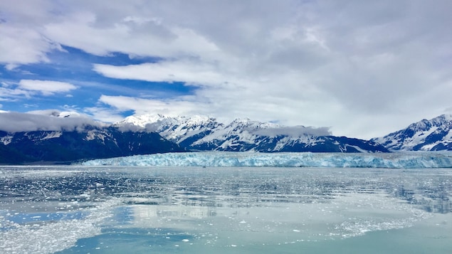 Un glacier et des montagnes couvertes de neige qui se reflètent dans l'eau.