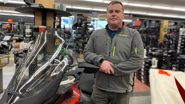 Joey Sutton pose, accoudé à une motoneige, dans son magasin.