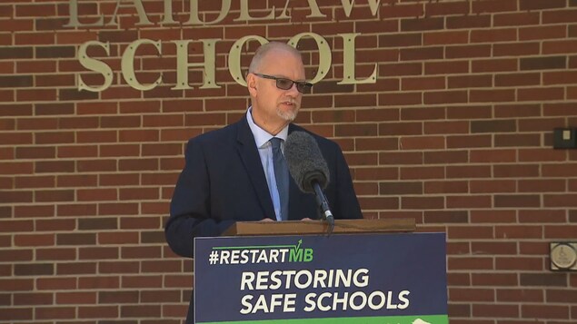 Le ministre de l'Éducation Kelvin Goertzen, au pupitre devant une école.