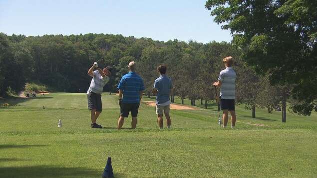 Quatre hommes de dos sur un terrain de golf
