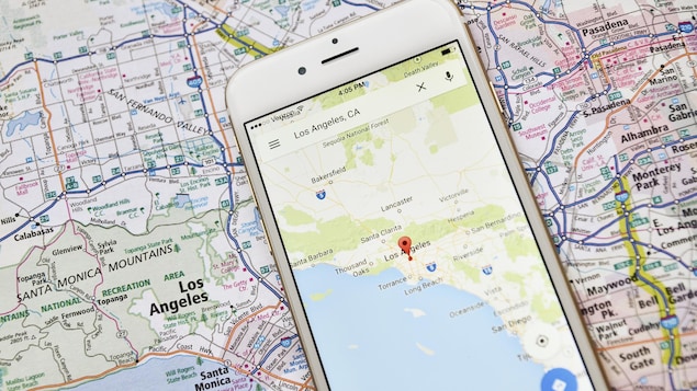 Une photo d'un téléphone déposé sur une carte géographique. L'écran du téléphone affiche une carte de la région de Los Angeles.