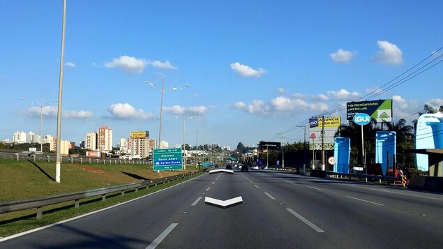 Vue sur une autoroute à trois voies, avec des panneaux de signalisation et de publicité en bordure de route.