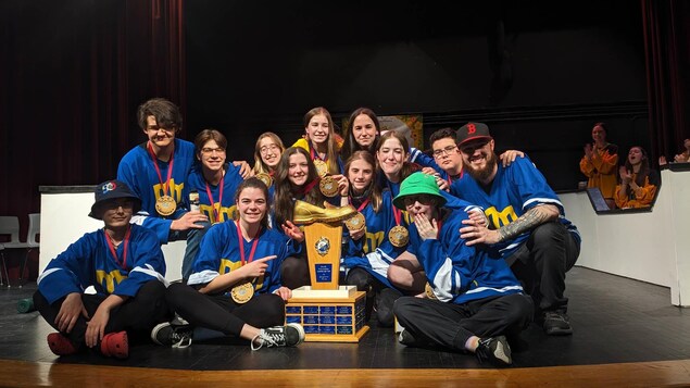 Treize personnes vêtues de chandails bleus et avec des médailles dorées au cou posent ensemble assis autour d'un trophée.