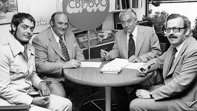 Quatre hommes assis dans un bureau s'apprêtent à signer un document. Quatre hommes assis dans un bureau s'apprêtent à signer un document.