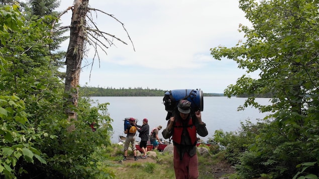 Des adolescents près d'un lac en forêt, avec des sacs à dos et des canots.