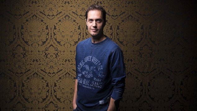 Grand Corps Malade pose debout et sourit.