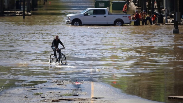 Un homme conduit son vélo dans les eaux au centre-ville de Grand Forks alors que des travailleurs installent des sacs de sable en arrière plan. Un homme conduit son vélo dans les eaux au centre-ville de Grand Forks alors que des travailleurs installent des sacs de sable en arrière plan.