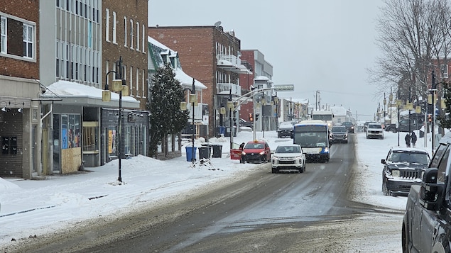 Une rue enneigée avec des commerces dont certains ont des vitrines placardées.