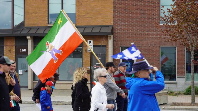 Un marcheur tient, dans la foule, un drapeau à l'effigie des Patriotes.