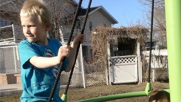 Un enfant blond en t-shirt sur une structure de jeux à l'extérieur. Un enfant blond en t-shirt sur une structure de jeux à l'extérieur.