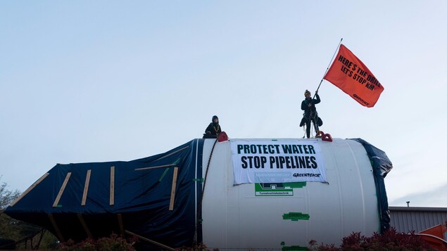 Deux femmes sur un tunnelier avec une affiche sur laquelle il est inscrit Protect Water, Stop Pipelines, ce qui signifie « Protégeons l’eau, arrêtons les pipelines ». Deux femmes sur un tunnelier avec une affiche sur laquelle il est inscrit Protect Water, Stop Pipelines, ce qui signifie « Protégeons l’eau, arrêtons les pipelines ».
