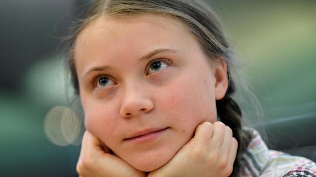 Greta Thunberg, vue de près, le visage entre les mains, regardant vers le haut.