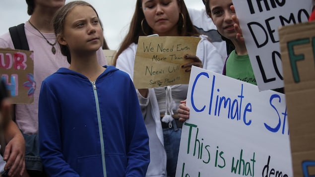 Greta Thurnberg est entourée de jeunes élèves tenant des pancartes pour la défense de l'environnement.