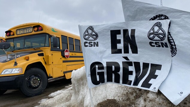 Des drapeaux de la CSN sur lesquels ont peut lire : en grève près d'un autobus.