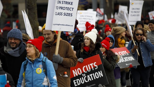 Des enseignants tiennent des affiches avec le message : « pas de coupes en éducation ».
