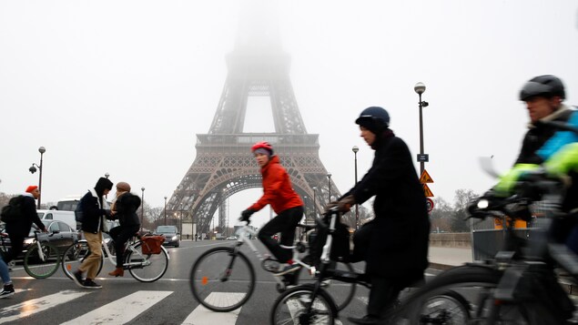 Des cyclistes et des piétons passent devant la tour Eiffel, enveloppée d'un brouillard opaque.