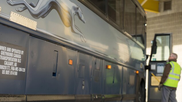 Le bus gris de la compagnie avec l'employé au second plan, flou, avec son gilet fluorescents jaune.
