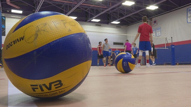 Un ballon à l'avant-plan, devant un entraînement de volleyball.