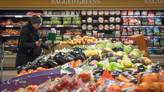 A woman inspects cucumbers in the produce section of a grocery store.