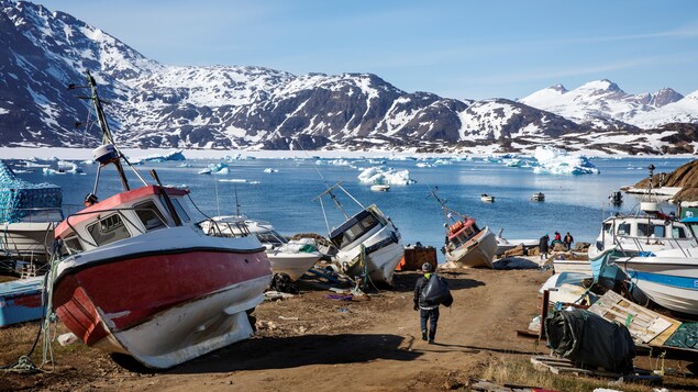 Un paysage du Groenland où l'on retrouve des bateaux, une étendue d'eau et des montagnes.