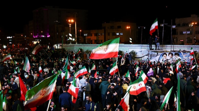 Des drapeaux iraniens flottent au-dessus d'une foule.