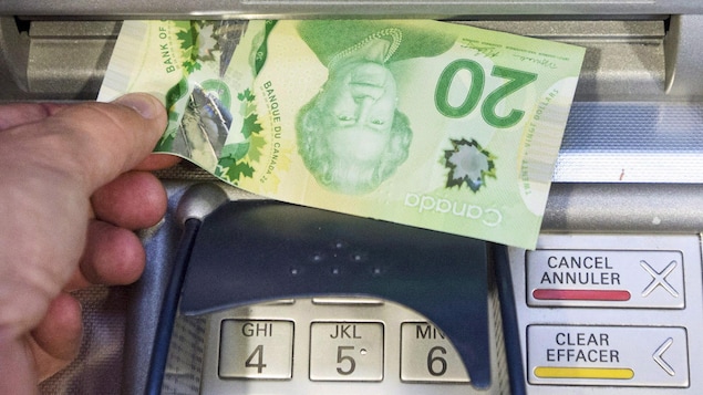 Un homme retire un billet de 20 dollars d'un guichet automatique.