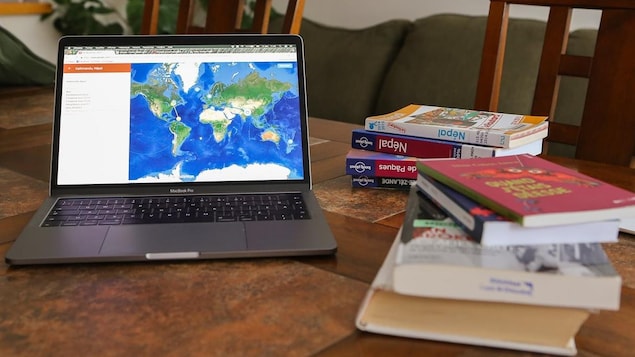 Un ordinateur affichant une carte du monde sur son  écran et des guides de voyage sont posés sur une table. 