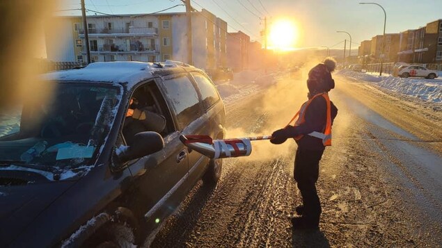 Une personne récolte le don d'un automobiliste grâce à une tirelire au bout d'une perche.