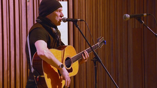 un homme, la guitare à  la main est devant un micro.
