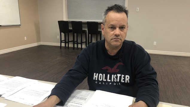 Homme à l'air sérieux avec documents sur une table devant lui.