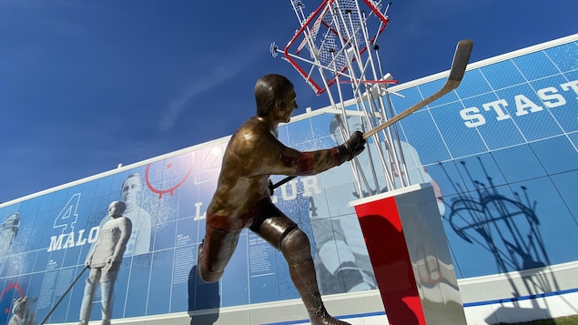 Devant une statue de bronze de Guy Laleur, une trainée de rondelle défoncent un filet accroché dans les airs.