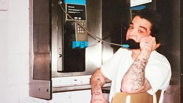 Un homme du nom de Guy Langlois est assis sur une chaise et tient le combiné d'un téléphone public.