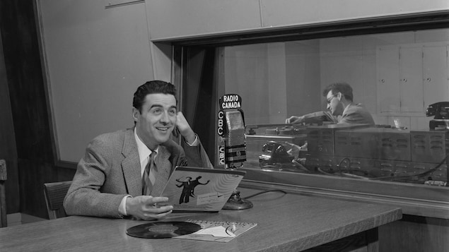 Guy Mauffette, en studio radio, souriant, un vinyle à la main.