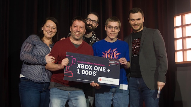 Une photo de Marie-Ève Pageau, Éric Letarte, Jean-Sébastien Daigle, Frédérick Capovilla et Maxime St-Pierre. Éric Letarte et Frédérick Capovilla tiennent une affiche sur laquelle ont peut lire « Grand prix Médias numériques, Xbox One + 1000 $ ».