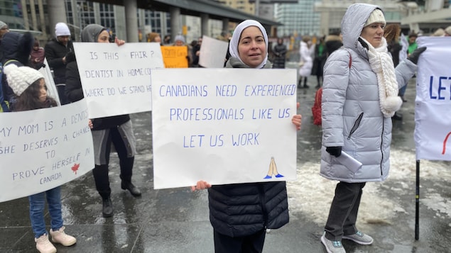 Une femme tient une pancarte qui dit "les Canadiens ont besoin de professionnels expérimentés comme nous. Laissez-nous travailler».