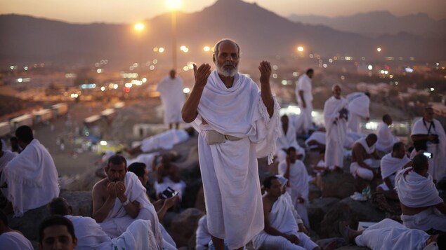 Vêtu d'un toge blanche, un pèlerin musulman prie au mont Arafat en levant les mains. Il est entouré de dizaine d'autres croyants. Vêtu d'un toge blanche, un pèlerin musulman prie au mont Arafat en levant les mains. Il est entouré de dizaine d'autres croyants.