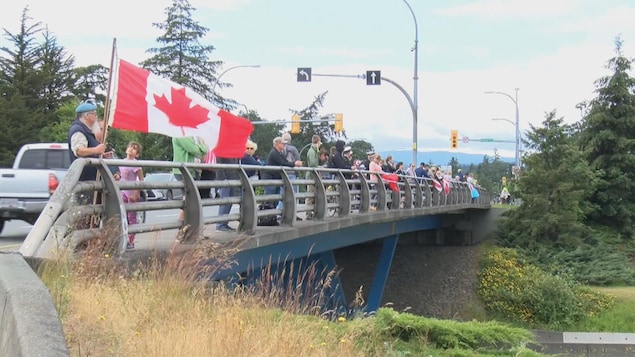Des dizaines de gens rendent un dernier hommage au capitaine Hagen debout sur un pont dans le Grand Victoria.