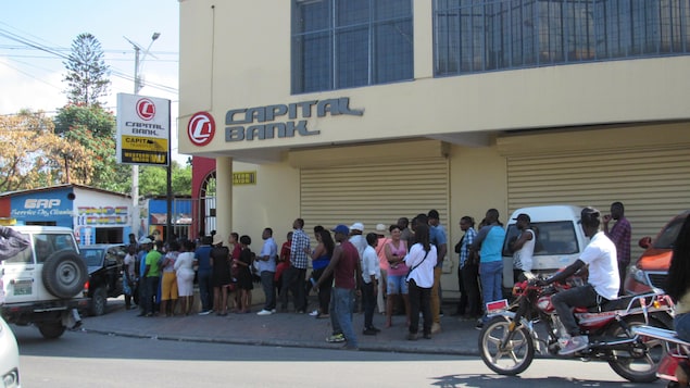 Plusieurs personnes attendent les uns derrière les autres devant un bâtiment sur lequel il est écrit: «Capital Bank».
