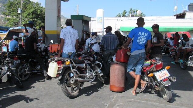 Des hommes avec leur motocyclette font la file à une station service en plein jour.