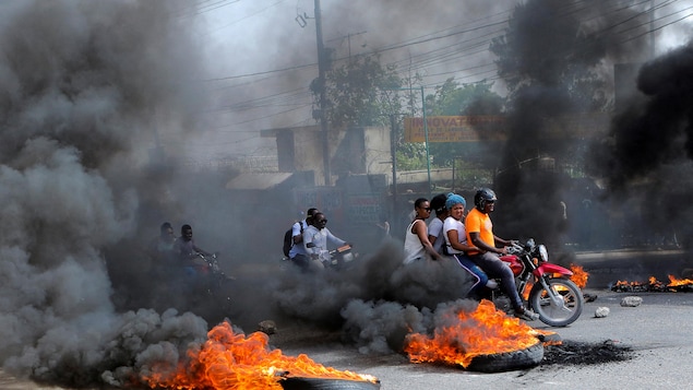 Des Haïtiens à moto entre des pneus qui flambent.