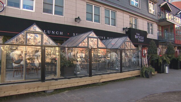 Trois petites serres pleines de convives sur la terrasse d'un restaurant.