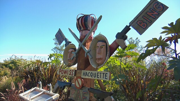 Une sculpture en bois représentant des têtes d'homme et des armes à feu dans un parc.
