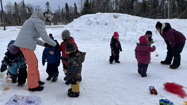 Les enfants jouent dans la neige avec deux éducatrices.