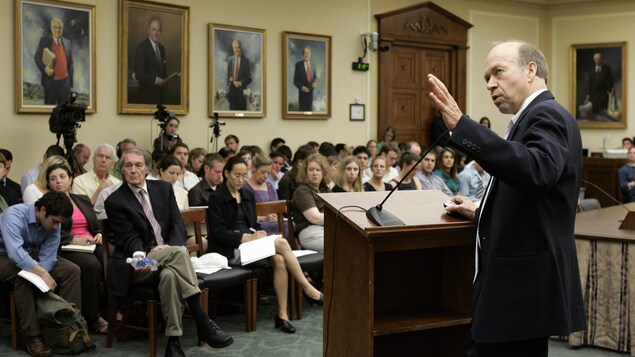 James Hansen, debout derrière un lutrin, semble désigner quelque chose derrière lui alors qu'il s'adresse à plusieurs personnes assises devant lui dans une pièce du Capitole de Washington.