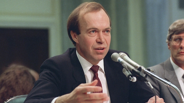 Une photographie d'archive datant de 1989 illustre James Hansen parlant devant deux micros.