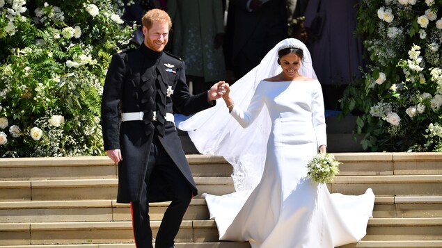 Un homme vêtu d'une veste noire et une femme portant une robe de mariée descendent les marches d'une église. 