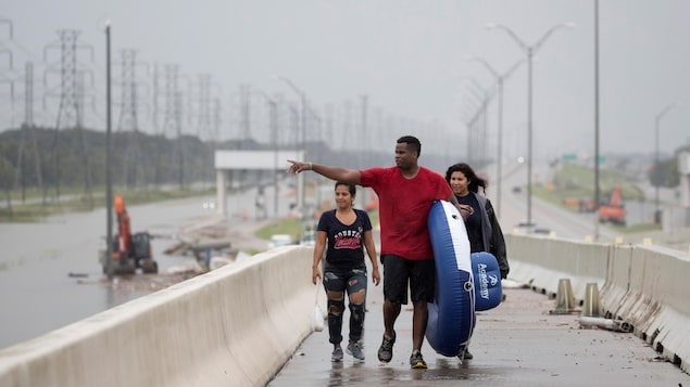 Trois personnes marchent sur une autoroute inondée, au Texas.