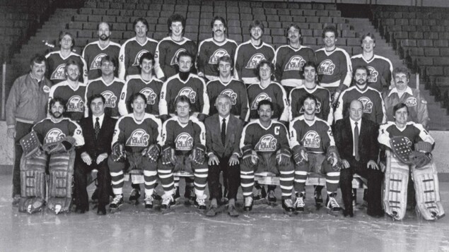 Une photo d'équipe en noir et blanc des joueurs de hockey des Hawks, prise sur la patinoire de l'aréna.