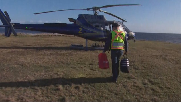 Un homme de dos transporte des sacs jusqu'à un hélicoptère.