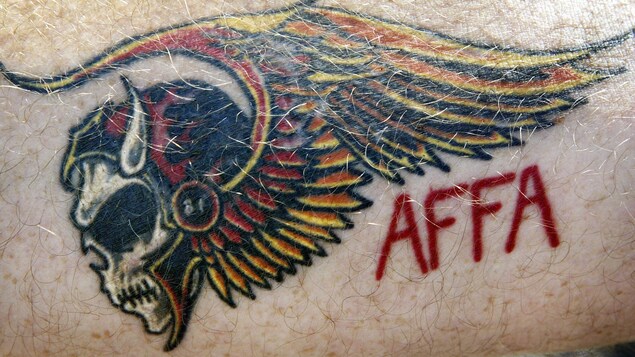 Le tatouage représente une tête de mort ailée, accompagnée de l'acronyme « AFFA ». Le tatouage représente une tête de mort ailée, accompagnée de l'acronyme « AFFA ».